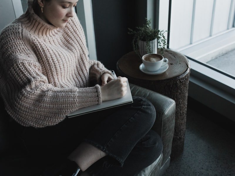Mujer escribiendo en un cuaderno junto a una ventana